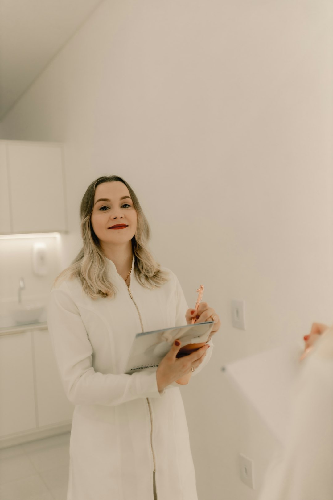 Woman in lab coat holds pen and tablet in a modern clinic.